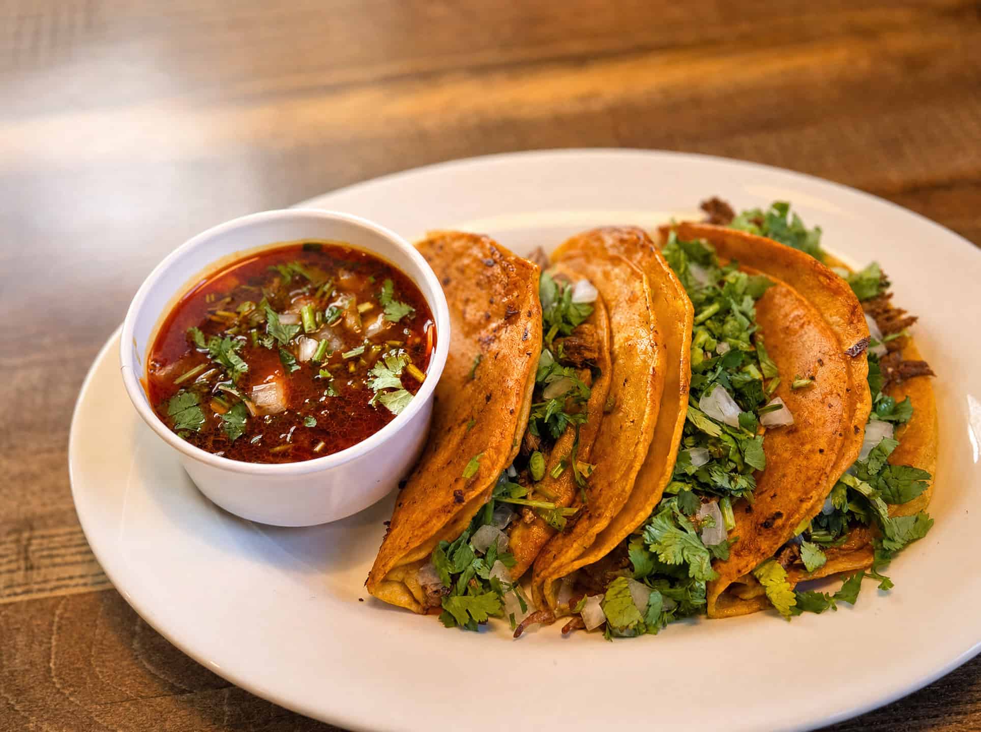 Quesabirria tacos with cilantro, onion, and a cup of consomme